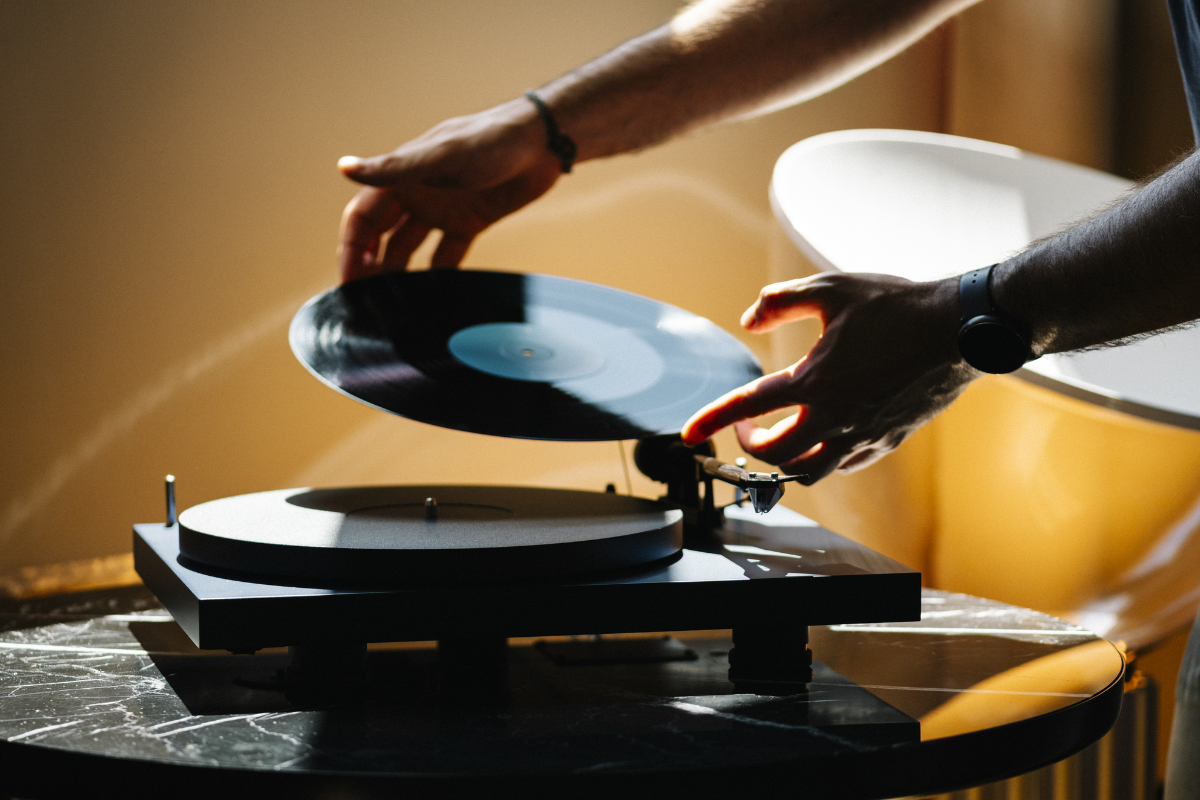 Eine Person legt eine schwarze Schallplatte auf einen Plattenspieler, der auf einem runden Marmortisch steht