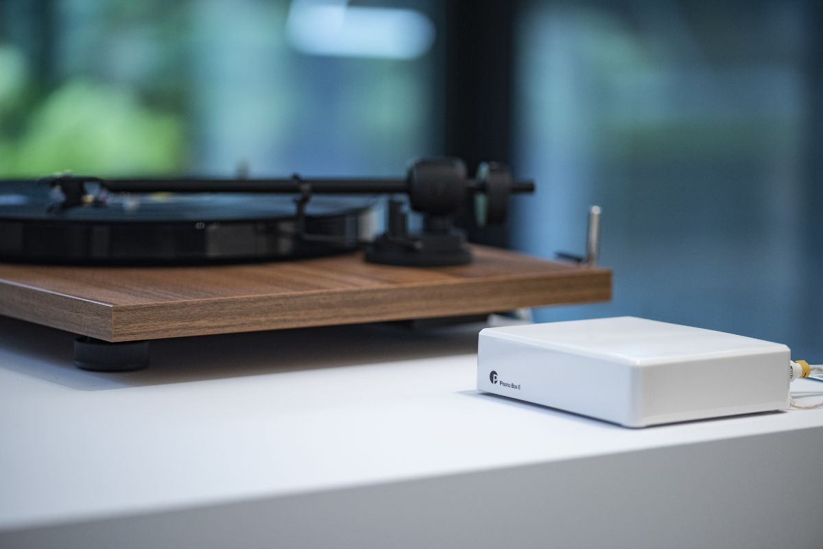 Moderner HiFi-Plattenspieler aus Holz auf einem weißen Sideboard, daneben ein kompakter weißer Vorverstärker in einem hellen Wohnraum.