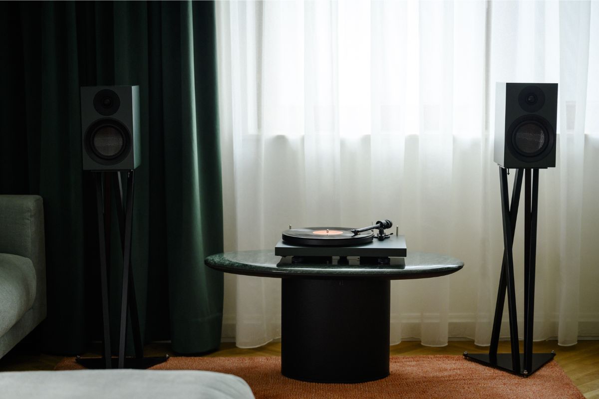 Schwarze Hi-Fi-Lautsprecher auf Ständern flankieren einen Plattenspieler auf einem Marmortisch vor einem großen Fenster