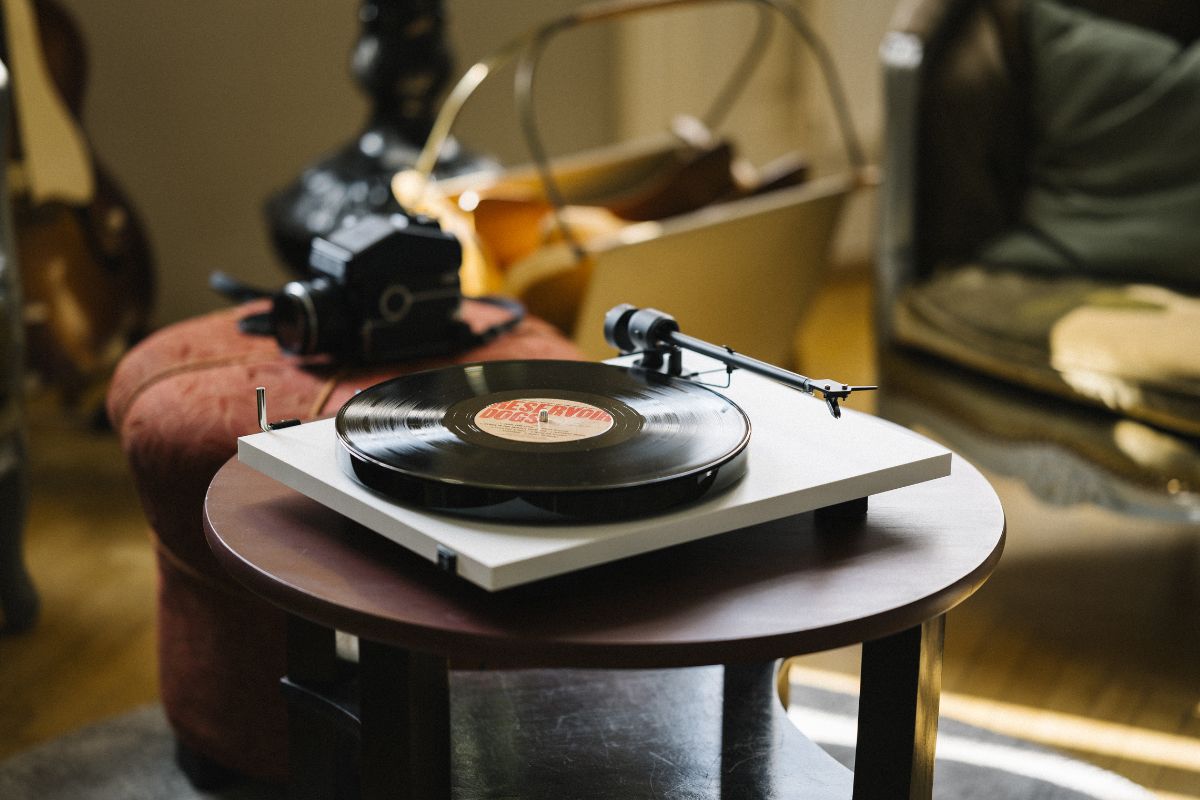 Weißer Plattenspieler mit aufgelegter Vinylschallplatte auf einem kleinen Holztisch in einem gemütlichen Wohnzimmer.