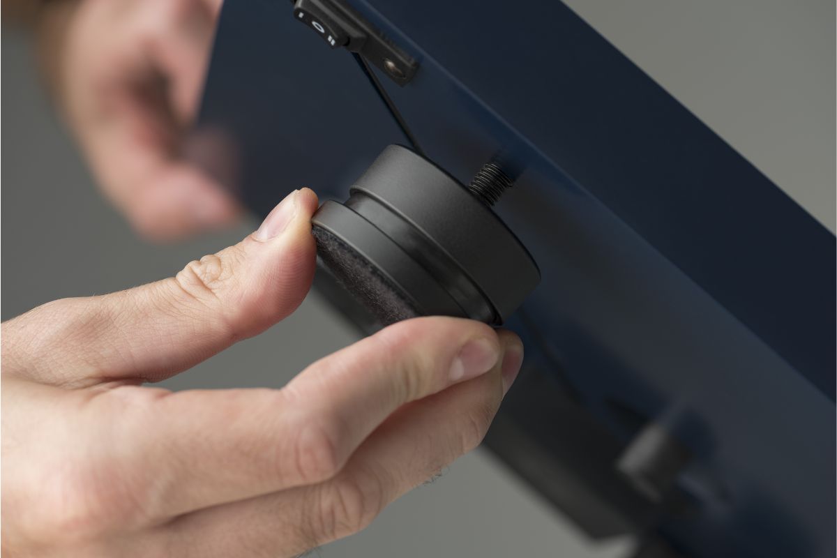 Hand hält einen runden Plattenspielerfuß und justiert ihn an der Unterseite eines Geräts