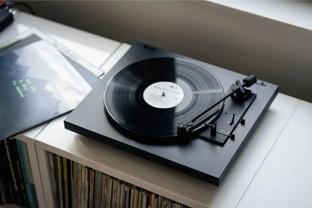 Schwarzer Plattenspieler Pro-Ject A1.2 mit Vinyl-Schallplatte auf einem weißen Regal, daneben liegen weitere Schallplatten