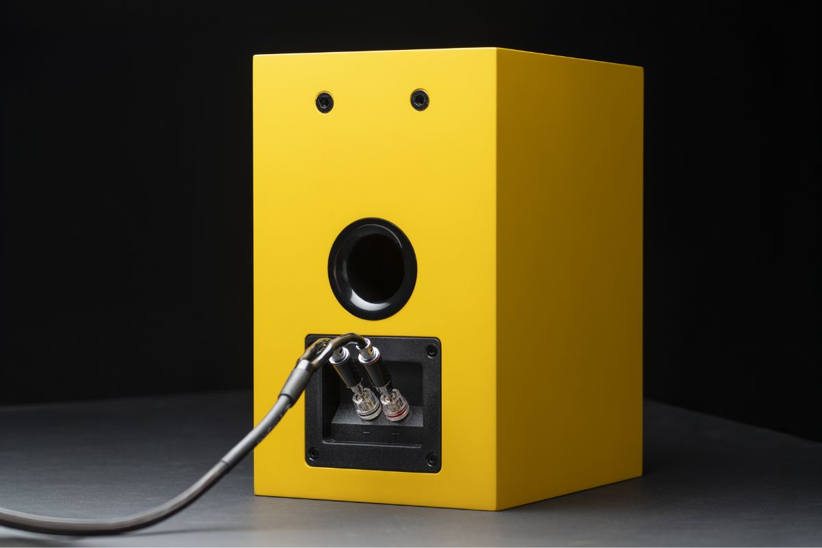 Rückseite eines gelben HiFi-Lautsprechers mit angeschlossenen hochwertigen Lautsprecherkabeln und Bassreflexöffnung